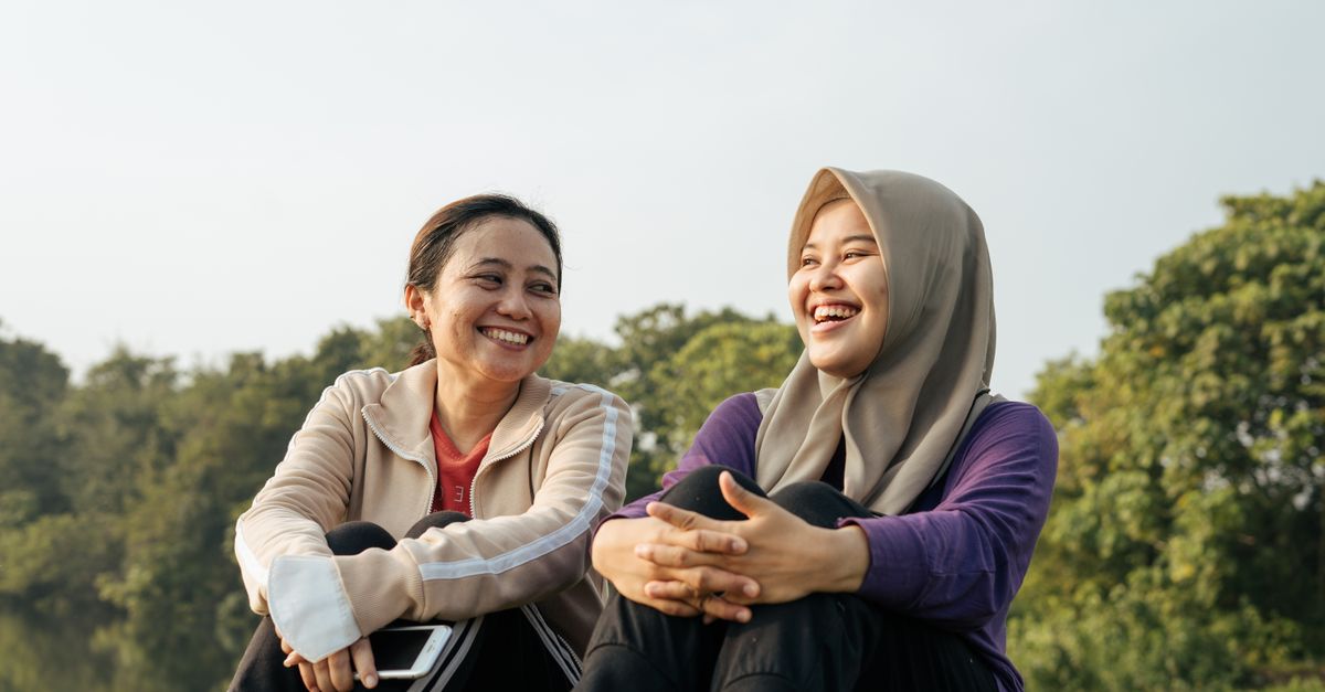 Two women laughing together outdoors, capturing a moment of friendship and happiness.